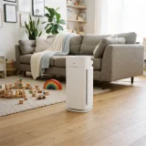 asset_04cf2fef4d49b64e Winix C610 air purifier on the floor of a bright playroom with wooden toys scattered nearby