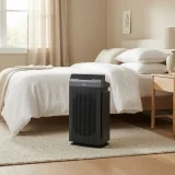 A Winix 5300-2 air purifier beside a neatly made bed in a calm sunlit bedroom