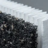 asset_086b19d32195a750 Close-up of the black carbon filter layer sitting ahead of white pleated True HEPA media