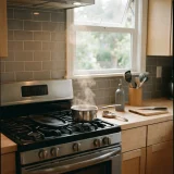 Home kitchen with light cooking haze above a stove and a window vent open