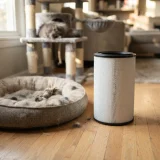 asset_1cacca3509d0ec0a Cylindrical filter beside a dog bed on a living room floor with a cat tree blurred behind