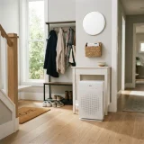 asset_1d4ad01d6636e601 Winix C909 air purifier placed near a home entry hall with coats and shoes on a rack