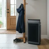 A Winix 5300-2 air purifier standing in a home entryway beside a coat rack and shoes