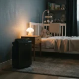 Winix 5500-2 air purifier on a low setting beside a small bed in a dim nursery