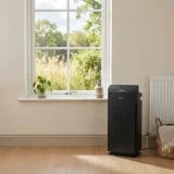 Winix 5510 air purifier beside a closed living room window with tall grass and trees visible outside