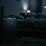 Winix 5500-2 air purifier glowing softly beside a bed in a dark room at night