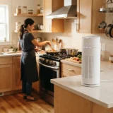 asset_31706bc1eb6e2579 Winix C535 air purifier running at the edge of an open kitchen while a person cooks at the stove in the background