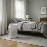 asset_3464535c3ff40a40 Winix C909 air purifier standing beside a bed in a calm, softly lit bedroom