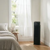 Winix 5510 air purifier running beside a sunlit bedroom window with sheer curtains and visible daylight