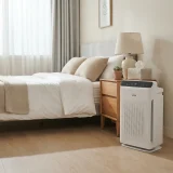 asset_3b7bdcedc4284b0f Winix C535 tower air purifier running beside a made bed in a sunlit bedroom with a tissue box on the nightstand