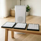 Winix AM90 air purifier beside a set of replacement filters arranged on a wooden table