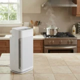 Winix AM90 air purifier on a tiled kitchen floor with a steaming pot on the stove behind it