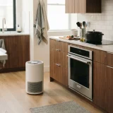 A white air purifier running on a kitchen floor beside counters with a covered pan