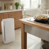 Winix AM90 air purifier on a kitchen floor beside a skillet of cooking food on the stove