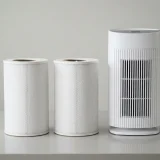asset_6121d8a044f468d3 Two round All-in-One replacement filters standing beside the Winix C610 air purifier