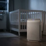 asset_6a75974a0d3d364d Winix T810 running with a dimmed indicator beside a crib in a darkened nursery.