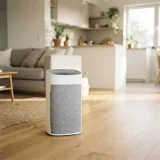 A Winix A230 air purifier on the floor of a small open-plan apartment living area with a sofa behind