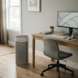 A Winix air purifier on the floor beside a home-office desk with a monitor and an office chair