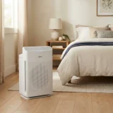 asset_8f995c10b4b9a77e Winix C545 air purifier running beside a bed in a softly lit bedroom
