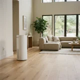 A tall white air purifier running in a spacious living room with sofa and large windows.