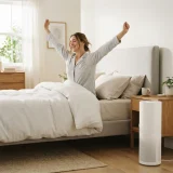 asset_99a5afee3e1f95d7 One adult sitting up in bed in the morning beside a Winix C535 air purifier