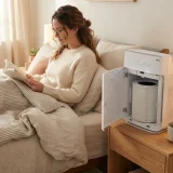 asset_9cb83dd1640188f9 Adult woman reading in bed beside a Winix C610 air purifier running with a fresh Filter Z canister
