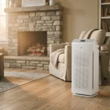 Winix Zero air purifier in a living room with a low stone fireplace and faint smoke haze