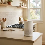 asset_b6ebd16fc49ad070 An air purifier on a kitchen counter near a stove with daylight from a window.