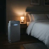 asset_b9a7345d72452020 Winix C545 air purifier glowing softly beside a bed in a dark bedroom at night