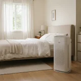 asset_bbc28305923d4bd5 Winix C610 air purifier running beside a bed with white bedding in a sunlit bedroom