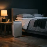asset_bea74111b3b982ba Winix C909 air purifier beside a neatly made bed in a dim bedroom at night