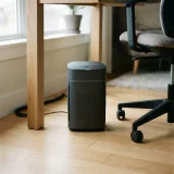 A Winix A230 air purifier on the floor beside a desk leg and office chair in a small home workspace