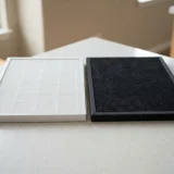 asset_d520a752cac28371 White pleated True HEPA filter and black carbon filter resting side by side on a light kitchen counter