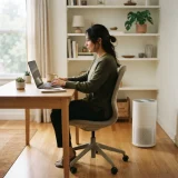 asset_de63a1a3181cbe23 One adult working on a laptop at a desk beside a Winix C535 air purifier in a home office