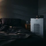 asset_e46af3072441d91c Winix C535 air purifier glowing faintly in a dark bedroom at night beside a sleeping area