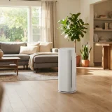 asset_f66586ceaad4f588 Winix C909 white tower air purifier running in a sunlit open-plan living room with sofa and plants