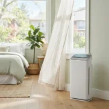 Winix air purifier running beside a window with open curtains